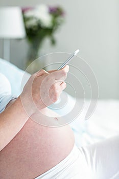 Pregnant woman lying in bed texting