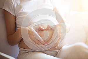 Pregnant woman lying in bed and touch her belly. Pregnancy heart shape at home, love sign