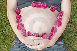 Pregnant woman lying on the grass. Her belly is adorned with little red flowers