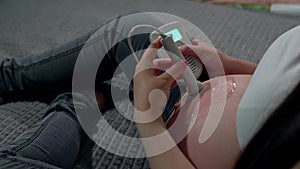 A pregnant woman lying in her bed at home uses a device to listen to her baby's heartbeat