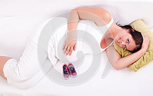 Pregnant woman lying on the sofa in front of baby boots.