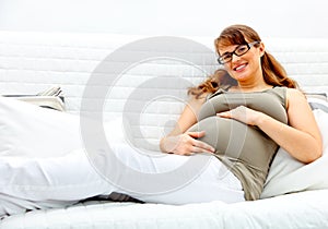 Pregnant woman lying on sofa and holding her belly