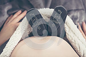 Pregnant woman lying on the sofa and holding shoes unborn child.