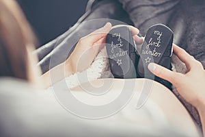 Pregnant woman lying on the sofa and holding shoes unborn child.