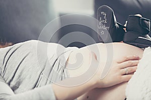 Pregnant woman lying on the sofa and holding shoes unborn child.