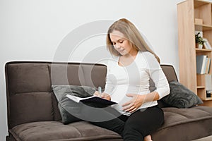 Pregnant woman lying on the sofa and making notes in her diary she resting at home