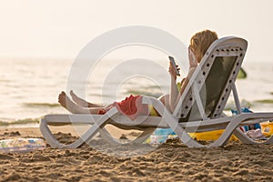 Pregnant woman lying on a sun lounger on beach and looking at the phone