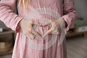 Pregnant woman makes heart shape with fingers on belly, closeup