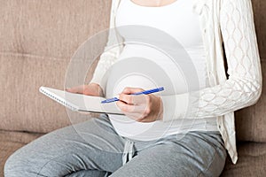 Pregnant woman makes notes. Concept of pregnancy, health care, medicine. Mother waiting of baby at the home