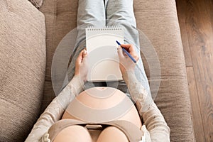 Pregnant woman makes notes. Concept of pregnancy, health care, medicine. Mother waiting of baby at the home