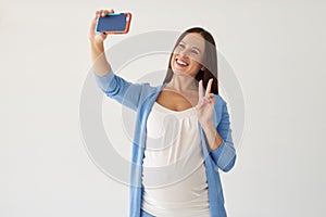 Pregnant woman making selfie against white background