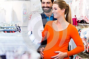 Pregnant woman and man buying baby clothes in store