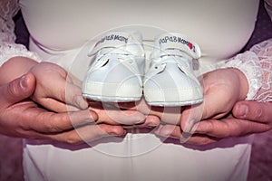 Pregnant woman and man holding baby shoes