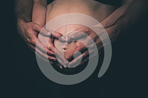 Pregnant woman and man holding heart shape on black background