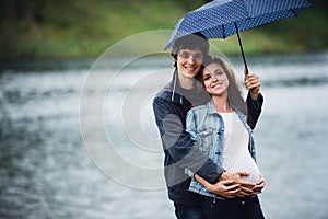 Pregnant woman and man holding an umbrella at the park in the drizzly day outdoors