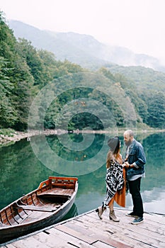 Pregnant woman and man stand on the pier by the lake near a moored boat