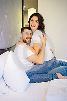 a pregnant woman and a man in white T-shirts and jeans on bed.