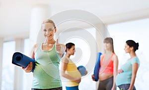 Pregnant woman with mat in gym showing thumbs up