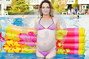 Pregnant woman with mattress near swimmimg pool