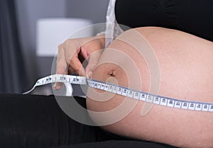 Pregnant woman measuring belly with measure tape