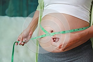 Pregnant woman measuring her belly with tape measure