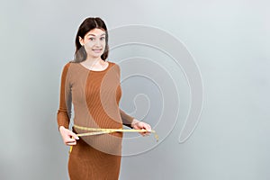 pregnant woman measuring her growing abdomen at colored background. Inch tape measure. Copy space