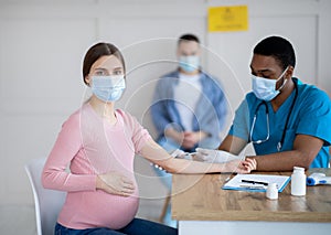 Pregnant woman in medical mask getting Covid-19 vaccine injection at hospital. Healthcare and vaccination concept