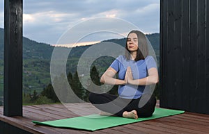 Pregnant woman meditating on house wooden patio at sunset view