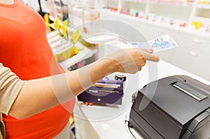 Pregnant woman with money at cashbox in drugstore
