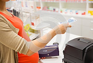 Pregnant woman with money at cashbox in drugstore