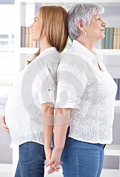 Pregnant woman and mother standing back-to-back