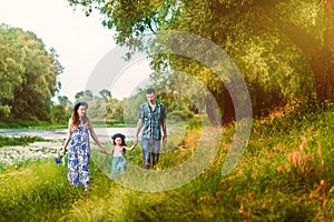 Pregnant woman mother to be in wreath and blue dress with her daughter and husband walking together near scenic river in sunset