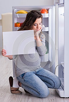 Pregnant woman near fridge with blank message
