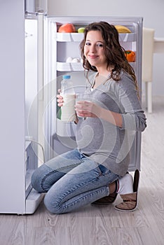 The pregnant woman near fridge looking for food and snacks