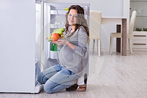 The pregnant woman near fridge looking for food and snacks