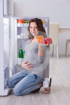 The pregnant woman near fridge looking for food and snacks