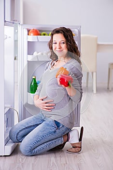 The pregnant woman near fridge looking for food and snacks