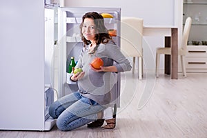 The pregnant woman near fridge looking for food and snacks
