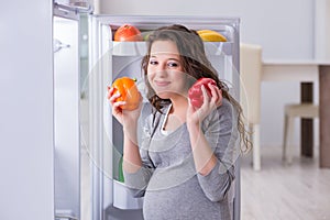 The pregnant woman near fridge looking for food and snacks