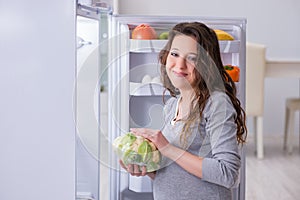 The pregnant woman near fridge looking for food and snacks