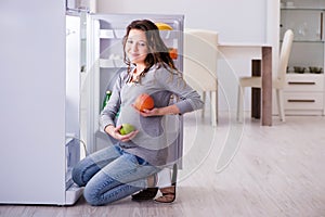 The pregnant woman near fridge looking for food and snacks