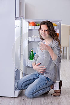 The pregnant woman near fridge looking for food and snacks