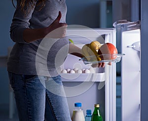 Pregnant woman near fridge looking for food and snacks at night