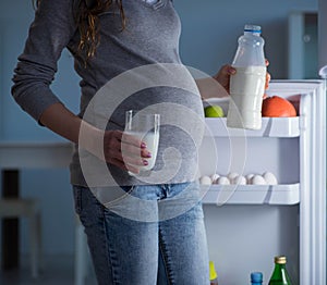 Pregnant woman near fridge looking for food and snacks at night