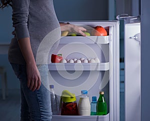 Pregnant woman near fridge looking for food and snacks at night