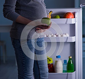 Pregnant woman near fridge looking for food and snacks at night