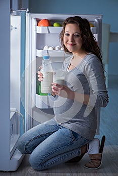 The pregnant woman near the fridge for snacks and food