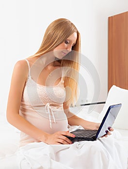 Pregnant woman in nightdress with laptop