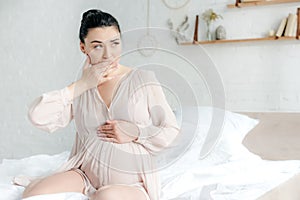 Pregnant woman in nightie having nausea while sitting on bed