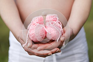 Pregnant woman outdoor with pink baby shoes in her hands